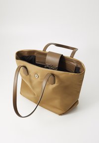Sac fourre-tout en nylon marron avec des accents en cuir, doté de deux poignées, d'une poche intérieure et d'une fermeture à pression. Doublure noire avec détail du logo.