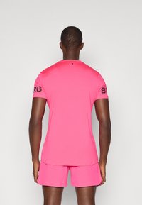 Lys rosa treningsskjorte med korte ermer og rund hals, med "BORG"-logo på venstre erme og glatt tekstilstruktur.