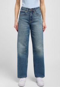 Light blue wide-leg jeans in denim fabric, featuring a high waist, five pockets, and subtle fading on the legs, paired with white sneakers.