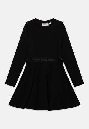 Zwart langemouwen jurk met een uitlopende rok, gemaakt van een gladde stof. Heeft een tailleband met het "Calvin Klein Jeans" logo in grijs.