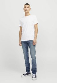 T-shirt blanche à manches courtes associée à un jean en denim bleu et des baskets bleu marine. La tenue est décontractée, avec une coupe slim et un minimum de détails.