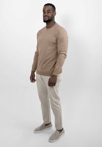 Lichtbruin gebreid vest met ronde hals, gecombineerd met crèmekleurige broeken en beige instappers. Soepele textuur, casual pasvorm en een minimalistisch ontwerp.