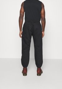 Svarta cargobyxor med elastiska manschetter, sidofickor och midja med dragsko, matchade med bordeauxfärgade stövlar. Strukturerad tyg, lös passform.