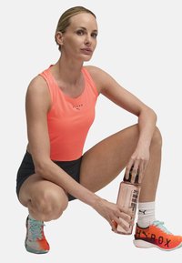 Neon orange athletic tank top with HYROX logo, black shorts, and multicolored sneakers. Holding a clear water bottle.