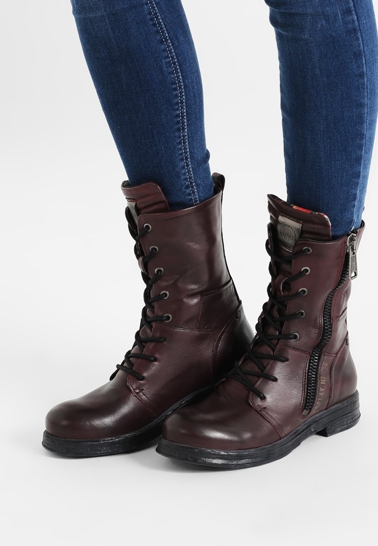 Stivali da combattimento bordeaux con lacci e cerniere laterali, indossati con jeans skinny blu, a dimostrare una scelta di calzature elegante e casual.