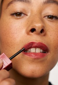 Rossetto liquido in una tonalità rosa scuro applicato con un applicatore. Caratterizzato da una texture liscia, un finish lucido e contorni delle labbra ben visibili.