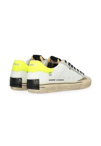 Sneaker bianchi in pelle con accenti neri e un dettaglio sul tallone in giallo neon. Presentano lacci neri e un logo sul lato. Suola usurata.