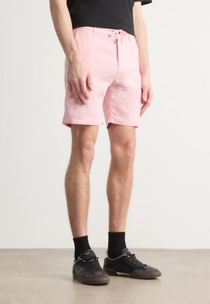 Lys rosa bomullsshorts med snøring i midjen, frontlommer og en avslappet passform, sammen med svarte sneakers og sokker.