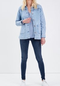 Jasnoniebieska kurtka dżinsowa z zapięciem na guziki, dwoma kieszeniami i luźnym krojem. Połączona z ciemnymi jeansami i białymi trampkami. Gładka faktura.