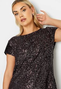 Musta paljettitoppi, jossa on pyöreä kaula-aukko, lyhyet hihat ja rento istuvuus. Korostaa pystysuoria paljetteja, jotka luovat tekstuurista ilmettä.