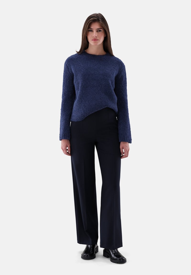 Navyblau gestrickter Pullover mit langen Ärmeln, kombiniert mit schwarzen weit geschnittenen Hosen und schwarzen Knöchelschuhen, auf einem Modell vor einem weißen Hintergrund präsentiert.