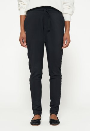 Pantaloni jogger neri realizzati in un tessuto liscio e elastico. Presentano una vita con cordino e dettagli laterali con testo stampato lungo la gamba.