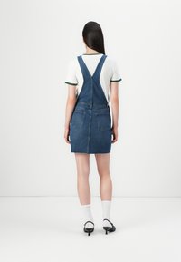 Nööriga denimitööd dress, millel on frayed serv ja kaks tagumist taskut, koos valge särgiga, millel on roheline ääre. 