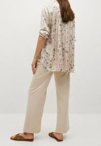 Lette blomstrede bluse i beige og grå med oprullede ærmer, parret med løse beige bukser og brune flade sandaler. Blødt materiale, afslappet pasform.