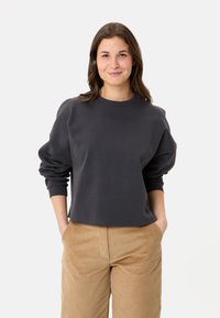 Felpa corta grigio scuro con scollatura rotonda, spalle scese e polsini a costine, abbinata a pantaloni in corduroy beige.