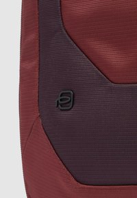 Rode en paarse rugzak met een gestructureerde stof en een zwart logo-accent. Het ontwerp bevat hoekige vormen en stiksel details.