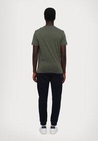 Olivengrønn t-skjorte med korte ermer, kombinert med marineblå joggebukser og hvite joggesko. Enkelt design; bomullsstoff, tettsittende form.