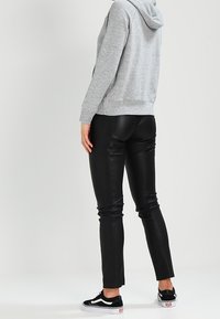 Sudadera gris con capucha de corte relajado, combinada con pantalones ajustados de cuero sintético negro. La modelo lleva zapatillas Vans en blanco y negro.