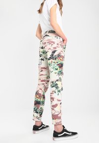 Mönstrade byxor i dämpad rosa och kräm med gröna blommiga accenter. Slim fit, avsmalnande ben och klassisk femficksdesign, kombinerade med svarta sneakers.