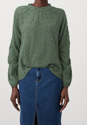 Groen topje met structuur, pofmouwen en een ronde halslijn, met verhoogde stippenpatronen. Gecombineerd met een denim rok met een voorste split.