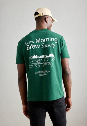 Groen katoenen T-shirt met drie cartoon koffie kopjes, tekst "Lazy Morning Brew Society" en een extra koffie-gerelateerde slogan eronder.