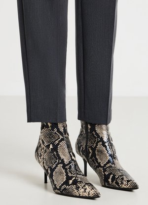 Spitz zulaufende High-Heel-Stiefeletten mit beigem und schwarzem Schlangenledermuster, getragen zu dunkelgrauen, maßgeschneiderten Hosen.