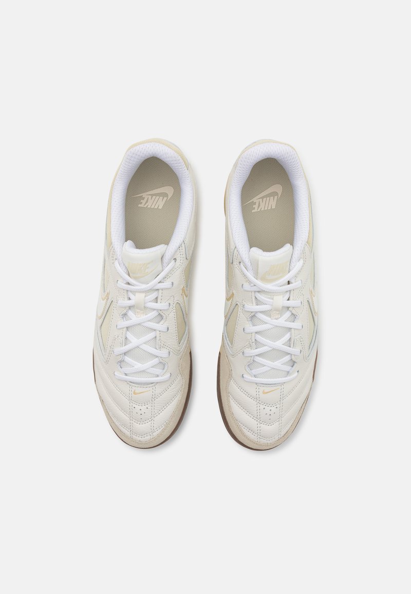 Zapatillas deportivas blancas con acentos beige, parte superior de tejido y sintético, detalles perforados, collar acolchado y suela de goma.