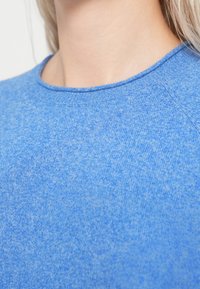 Μπλε πουλόβερ πλεκτό με υφή, στρογγυλή λαιμόκοψη και μανίκια raglan, που παρουσιάζει ένα απαλό μείγμα ανοιχτών και σκούρων μπλε αποχρώσεων.