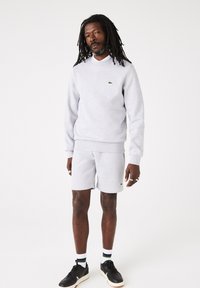 Grijze sweatshirt en shorts van zachte katoen met ribbelafwerking. Klein groen logo op de borst. Zwarte sneakers met witte accenten en gestreepte sokken.