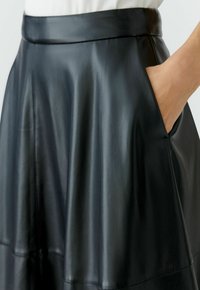 Schwarzer Lederrock mit glatter Textur, ausgestelltem Design, breitem Bund und seitlichen Taschen, die einen natürlichen Glanz präsentieren.