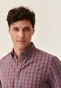Men's button-up shirt featuring a checkered pattern in navy and rust colors, classic collar, and small chest pocket. Cotton material with texture.