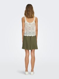 Débardeur en tricot blanc avec des détails ajourés et un ourlet festonné, associé à une jupe A-line vert foncé. Modèle portant des baskets blanches.