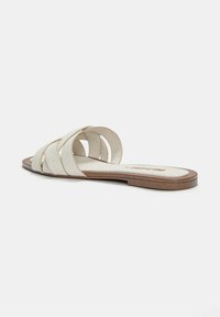 Sandales à glissière de couleur claire avec plusieurs lanières nouées, semelle plate et semelle intérieure texturée. Fabriquées en matériau doux avec une finition lisse.