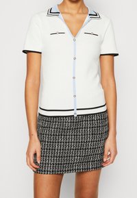 Witte top met korte mouwen, lichtblauwe kraag, zwarte afwerking en knoopaccenten; gecombineerd met een zwart-witte textuur minirok.