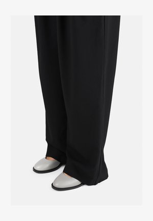 Laiad mustad püksid, millele on sobitatud heledast hallist nahast, avatud varbaga ja ümarate kujudega slip-on kingad, näidates sileda naha tekstuuri.