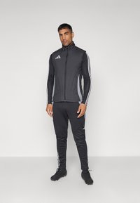 Chaleco atlético negro con cuello alto y cremallera, combinado con pantalones negros con franjas laterales. Hecho de tejido elástico con un diseño ajustado.