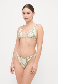 Zaļi un rozā ziedu bikini, kuram ir trīsstūrveida augšdaļa ar sasienamām siksnām un saskaņoti zemi izgriezti apakšdaļas ar sānu sasienamām siksnām un viļņainu rakstu.