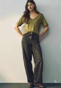 Olijfgroen v-hals t-shirt gecombineerd met hoge taille donkere denim jeans met een relaxte pasvorm, beide met een solide textuur. Bruine lederen schoenen.