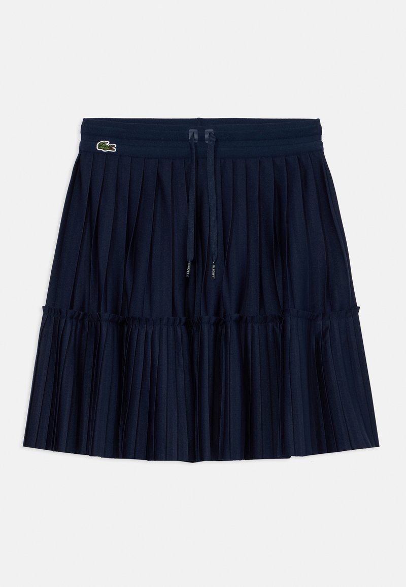 Jupe plissée bleu marine avec taille à cordon et petit logo crocodile vert en haut à gauche.