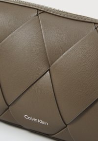 Clutch in pelle intrecciata marrone con texture trapuntata e ferramenta in tonalità argento. Presenta il logo Calvin Klein nell'angolo in basso.