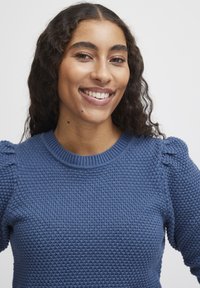 Blauer gestrickter Pullover mit einem strukturierten Muster, rundem Ausschnitt und Puffärmeln, der aus einem weichen Material gefertigt ist und eine figurbetonte Passform hat.