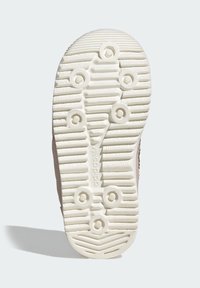 Svetlo hnede podrážka tenisky s textúrovanými žliabkami a kruhovými vzormi protišmyku. Obsahuje značku pozdĺž stredu a zaoblený dizajn špičky.