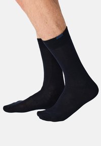 Mørkeblå bomuldssokker med ribstrikket manchet, midt på læggen, glat tekstur, forstærket tå og minimal brandingdetalje.