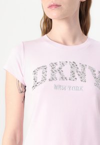 Fényes rózsaszín, rövid ujjú póló, ezüst flitterekkel díszített "DKNY" és "NEW YORK" felirattal a mellkasán. Puha pamut anyag.