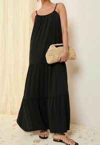 Svart maxiklänning med spagettiband, med en flerlagersdesign. Kombination med en vävd halmpåse och svarta sandaler med remmar.