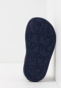 Sula på en sko, med ett mörkblått gummimaterial som har präglade djurmönster och "Camper"-logotyp.