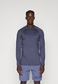 Langærmet, marineblå sports T-shirt med et tekstureret design, parret med lyseblå shorts med et mørkeblåt "BORG"-tryk på siden.