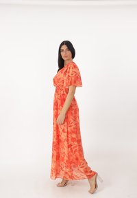 Maxiklänning i klar orange med blommönster, korta ärmar och elastisk midja, i kombination med klara klacksandaler.