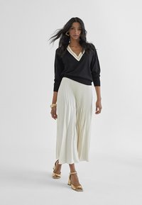 Black sweater with cream trim, pleated white skirt, and gold heeled sandals. The outfit features a relaxed design and flowing texture.