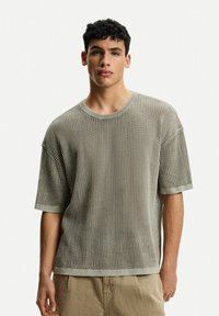 Light gray knitted t-shirt with loose fit, short sleeves, ribbed texture, and a round neckline. Features contrasting cuffs and hem.